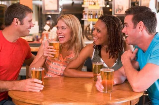 Quatre amis rient autour d'une table au bar en tenant des verres de bière