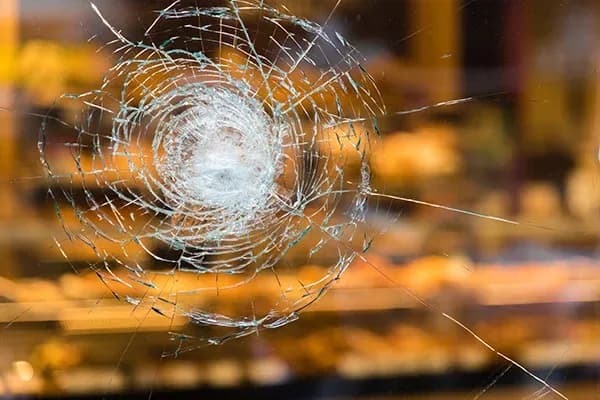 vitre brisée avec des fissures en étoile sur un fond flou de produits en vitrine