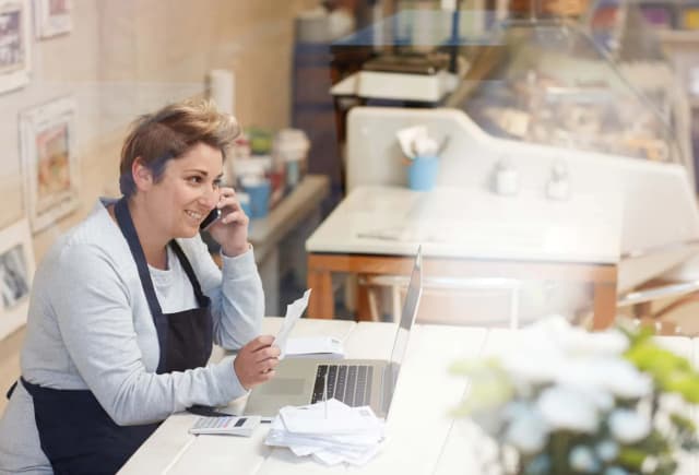 femme souriante au téléphone avec un ordinateur portable et des documents sur une table