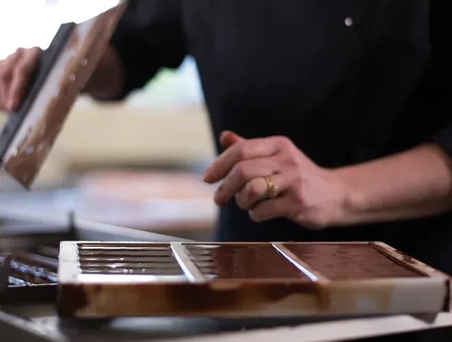 artisan chocolatier versant du chocolat dans un moule à pralines en atelier de fabrication