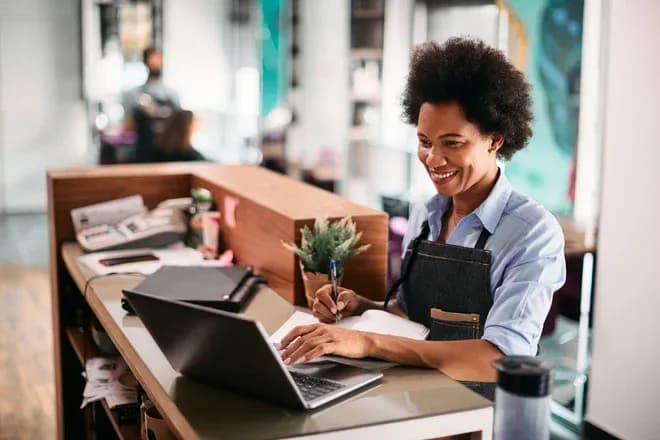 femme souriante utilisant un ordinateur portable dans un salon de coiffure moderne
