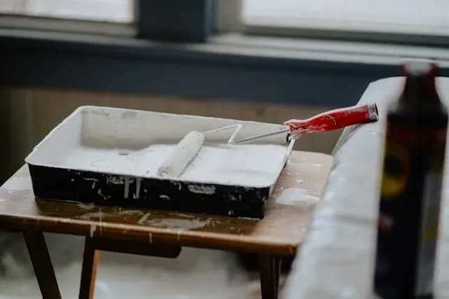 bac à peinture blanc avec rouleau rouge posé sur une table lors de travaux