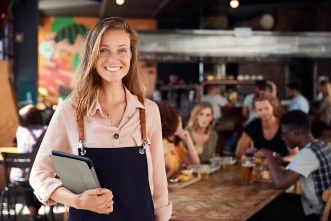 jeune gérante souriante tenant une tablette devant un restaurant animé