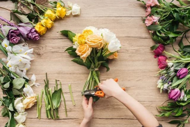main dans un bouquet de fleurs avec des tiges coupées sur une table en bois