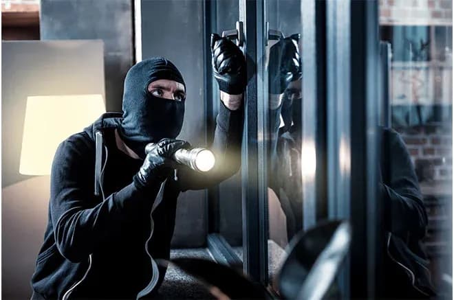 homme masqué avec une lampe de poche tentant d'ouvrir une fenêtre dans un intérieur sombre