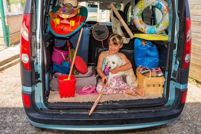 Préparation du trajet pour les vacances d'été : une petite fille rit dans le coffre entoure de bagages